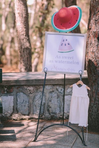 Welcome baptism sign with a watermelon slice and christening dress with crochet lace and pompoms.