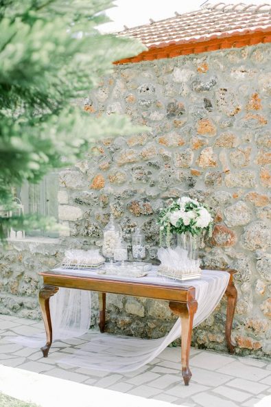 Wooden table with a white linen tablecloth, white flowers, and wedding favors in small organza bags.