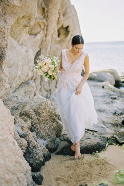 Sweet bride with blush and white wedding dress on the beach barefoot.