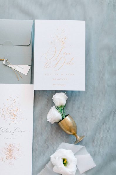 Detail shot of a minimal and chic wedding stationery in cream and gold colors and light grey background.