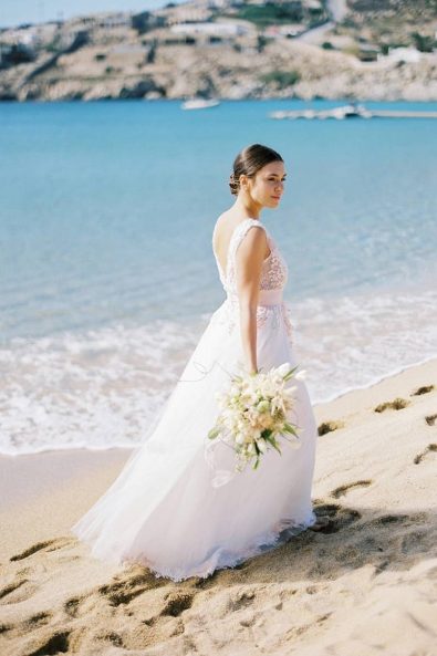 Bride walking barefoot in the sand wearing blush and white tulle wedding dress for a beach wedding in Mykonos.
