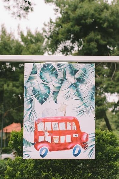 A decorative canvas with a red bus, jungle animals and green leaves print for a baby baptism.