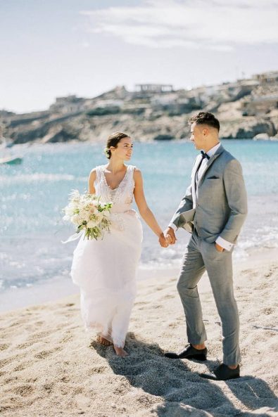 Couple walking on the sand for a destination beach wedding in Mykonos, Greece.