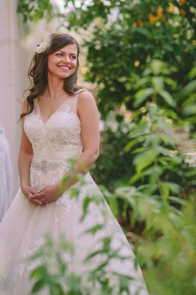 Elegant bride with a romantic lace wedding dress and loose waves hairstyle posing in a spring garden.
