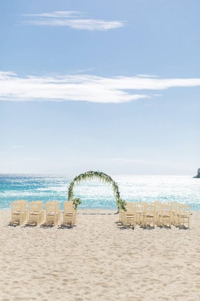 Beach ceremony styled shoot with wedding arch and wooden chairs on the sand, overlooking the Aegean sea.