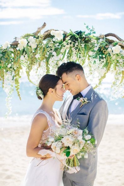 Loving couple looking at each other's eyes on the beach in front of the flower decorated altar.