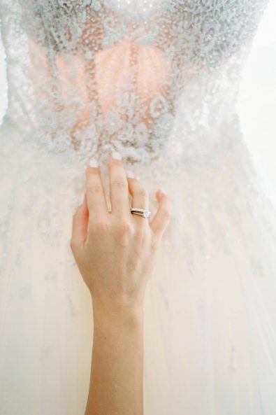 Close up of bride's hand with her wedding band and diamond engagement ring with her minimal and chic wedding dress as background.