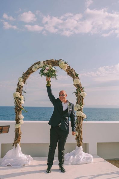 Groom eager to get married waving the bridal bouquet in the air while waiting for his bride at a destination wedding in kalamata.