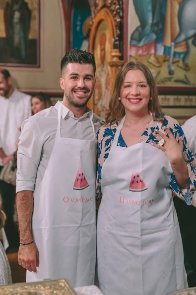 The godmother and the godfather wearing a white apron with watermelon print on it before they baptize the baby.