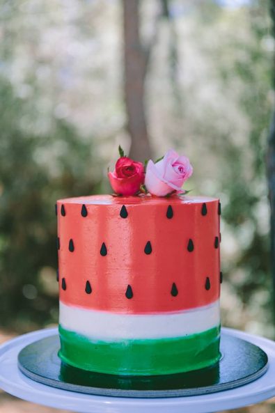 Watermelon red and green cake with black seeds and roses on top for a baptism ceremony.