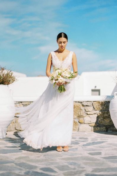 Stylish bride on the rooftop of a Greek island house holding her flowers.