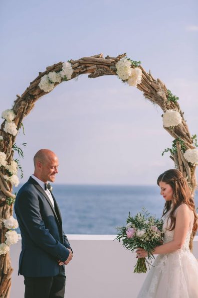 Bride and groom exchanging vows in the wedding arch overlooking the Mediterranean sea .