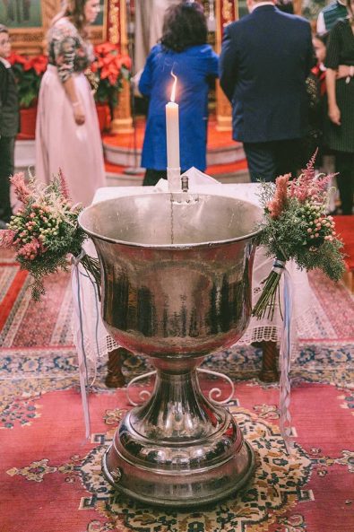 Silver church baptistery with winter flower arrangements and lit up christening candle.