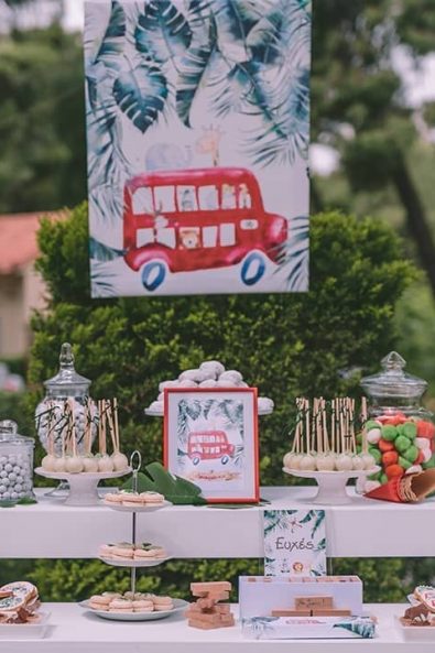 baby baptism candy bar with white tables, decorated with palm leaves and christening sweets such as biscuits, tarts, macarons, and marshmallows,