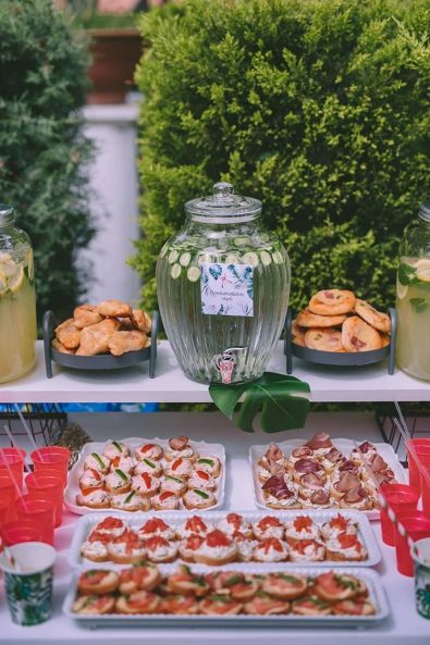 Savory treats buffet for a boy baptism party, with canapes, red plastic cups, and refreshing cucumber water.
