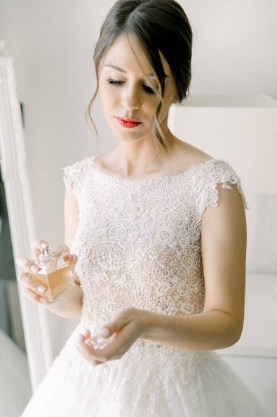 Portrait of a bride in a lace dress, low bun updo and red lipstick wearing Chloe roses perfume for her wedding day.