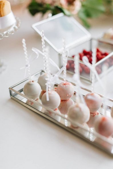 White chocolate covered cake pops with blush sprinkles on a silver gilded glass mirror tray.