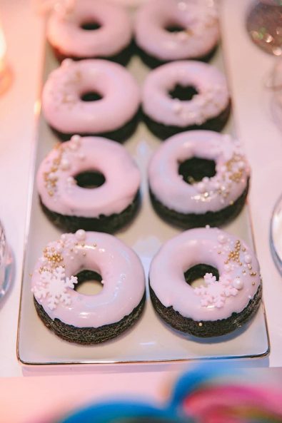 Pink glaze dipped chocolate doughnuts with snowflake and gold sprinkles.