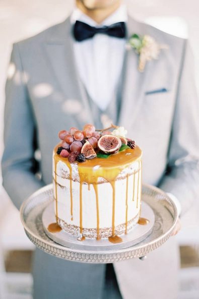 Fine art late summer naked wedding cake with caramel sauce and figs, grapes and berries on a silver tray.
