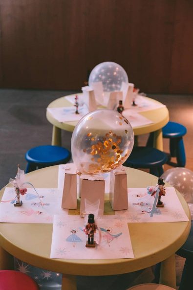 Children's table with custom-made placemats, small nutcracker ornament christening favor, confetti balloon, and light pink party favor paper bag with candy.