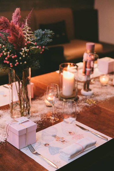 Close up shot of Nutcracker ballet inspired table setting, custom-made place mat with ballerinas and nutcracker, glitter snow and christening favor in a pink box.