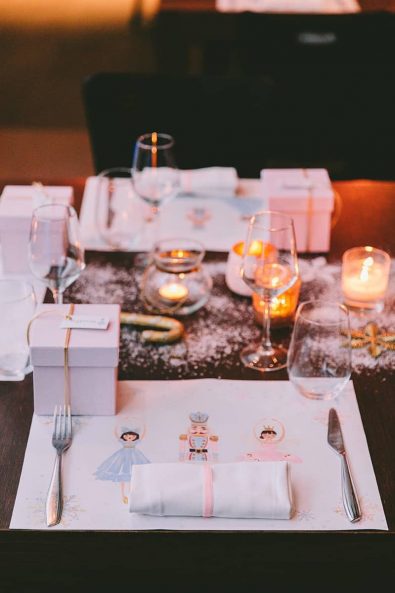 Baptism ideas - Close up shot of table setting with custom-made nutcracker placemats, crystal glasses, pink box baptism favor, glitter snow, and candles.