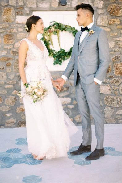 Bride in a wedding dress and groom in a grey suit wedding portrait looking at each other while holding hands.