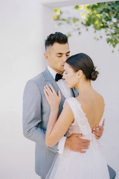 Romantic wedding couple photography with bride and groom in a sweet embrace with a white wall background on a Greek island.