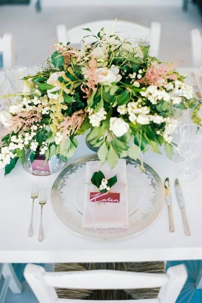 Romantic summer table setting with blush and cream flower centerpiece, elegant flatware and name cards in dark red marsala.