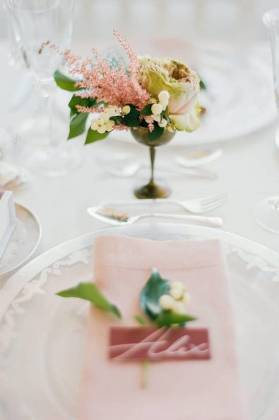 Close up shot of flowers in a vintage silver flower holder and table setting in pink shades.
