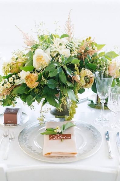 Fine art wedding table setting with flower centerpiece and cream pink linen napkins and elegant silver rimmed plates.