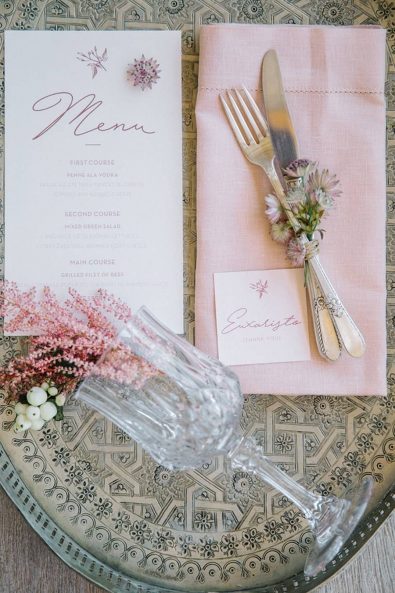 Reception menu with pink letters, pink linen napkins and silver flatware, and crystal glass on a vintage metallic serving tray.