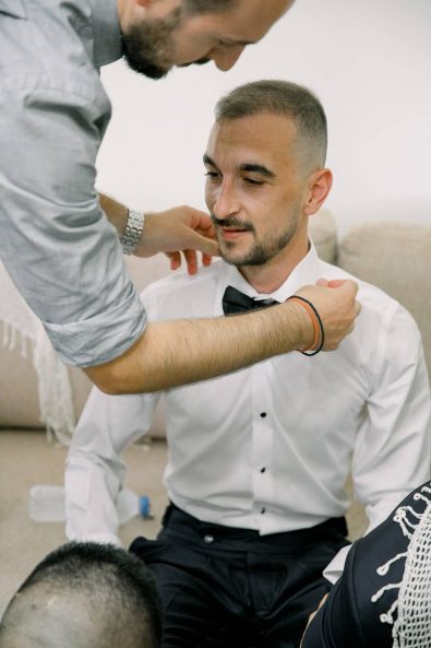 Portrait of the groom getting ready while his best man ties his bow tie.