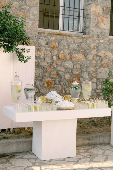 White and gold refreshments stand with lemonade and flavored water and almond sweets for wedding guests to enjoy after the ceremony.