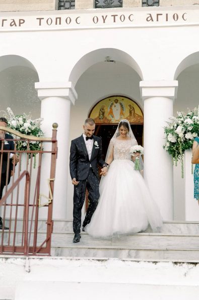 Bride and groom leaving the church hand in hand while the guests throw rice at them.