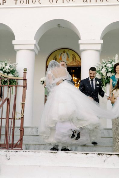 Groom carrying the bride down the church stairs while rice is being thrown at the minimal and chic wedding