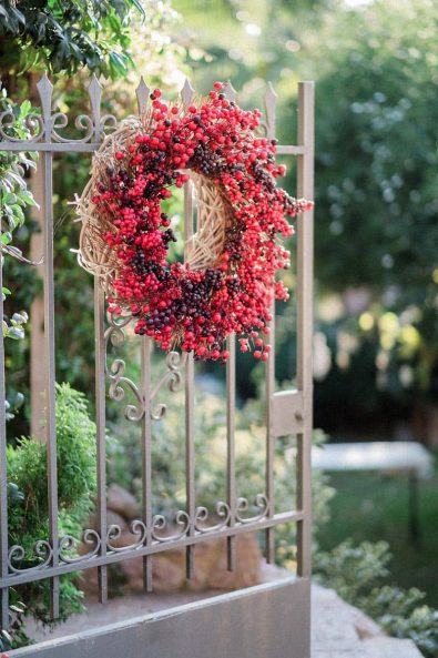Festive red and burgundy wreath hanging on an iron garden entry door.