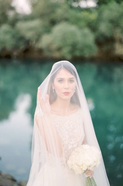 Portrait of a bride with a minimal and chic wedding tulle veil, red lipstick and white roses bouquet.