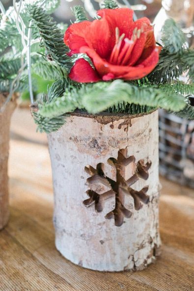 Wooden plant pot with a laser cut snowflake on it and a red flower inside.