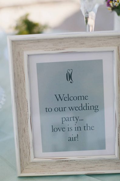 Love is in the air welcome wedding party sign in dusty blue in a wooden frame.