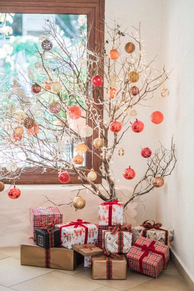 Christmas tree made from branches with gold, white and red baubles and presents wrapped in festive paper private Christmas dinner.