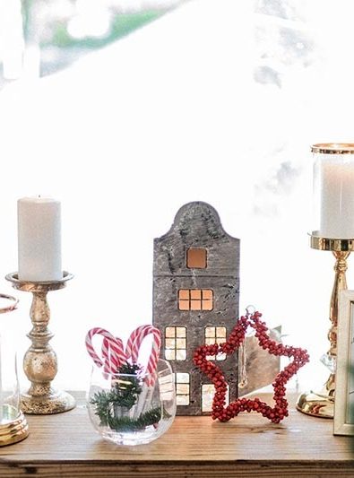Gold candle holders with white candles, candy canes, and star decoration in front of a large window at a private Christmas dinner.