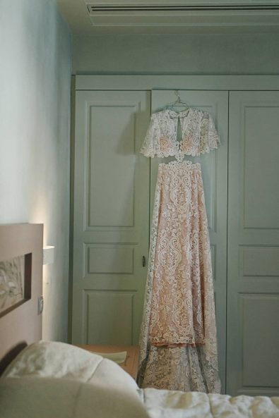 Boho cream white lace summer wedding dress hanging in front of a pistachio pastel green wardrobe.
