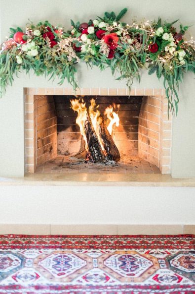 Christmas decorated fireplace with festive flowers, fairy lights, and baubles.