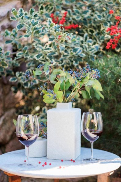 Glasses of red wine on a round white marble table and red mistletoe berries.