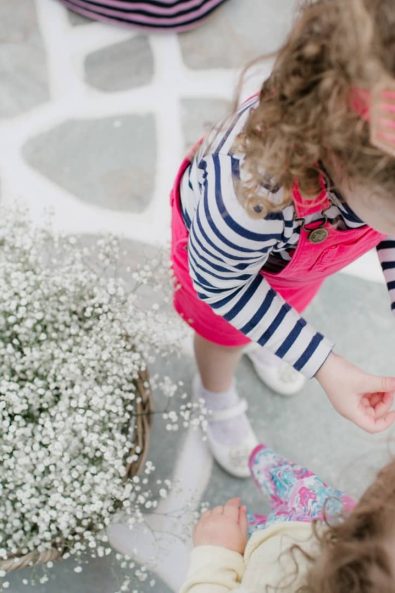 Girl toddlers with curly hair playing with each other next to a basket full of white flowers.