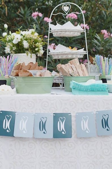 Party refreshments lemonade stand with homemade lemonade, colorful straws, paper cones filled with rice, hand fans and paper flags garland.
