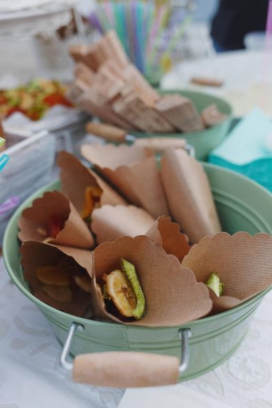 Craft paper cones filled with dried fruits in a sage green tin bucket for guests to enjoy.