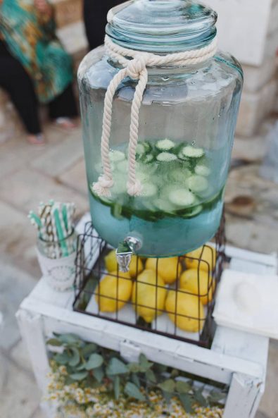 Cucumber flavored water jar with lemons decoration underneath and colorful straws in the side.