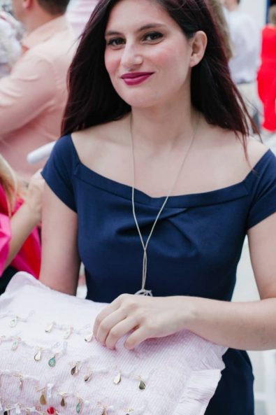 Beautiful girl in a blue dress holding a pink pillow with the christening pins on it.